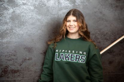 Student wearing a green crew neck sweater with the Nipissing Lakers logo across the front