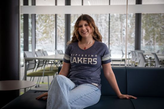 Student wearing a blue/grey v-neck tee with the Nipissing Lakers logo on the front