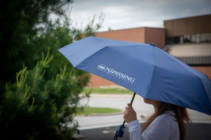 Student holding an umbrella with the Nipissing Alumni logo on the front