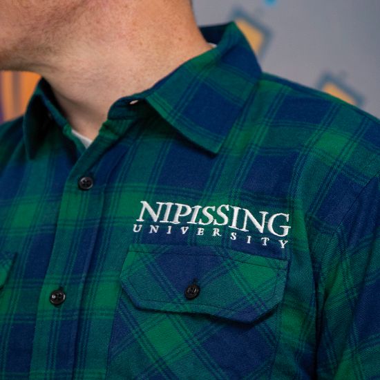 Man wearing a blue/green flannel shirt with "Nipissing University" logo on the front